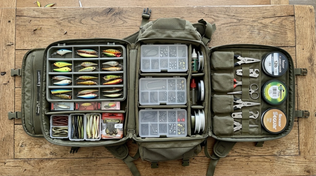 Angler organizing gear inside an all-in-one fishing backpack by a lake.
