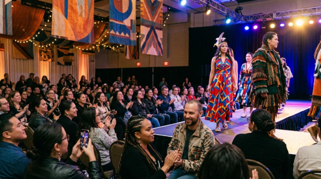 Audience watching a colorful Indigenous fashion show runway event in a decorated venue